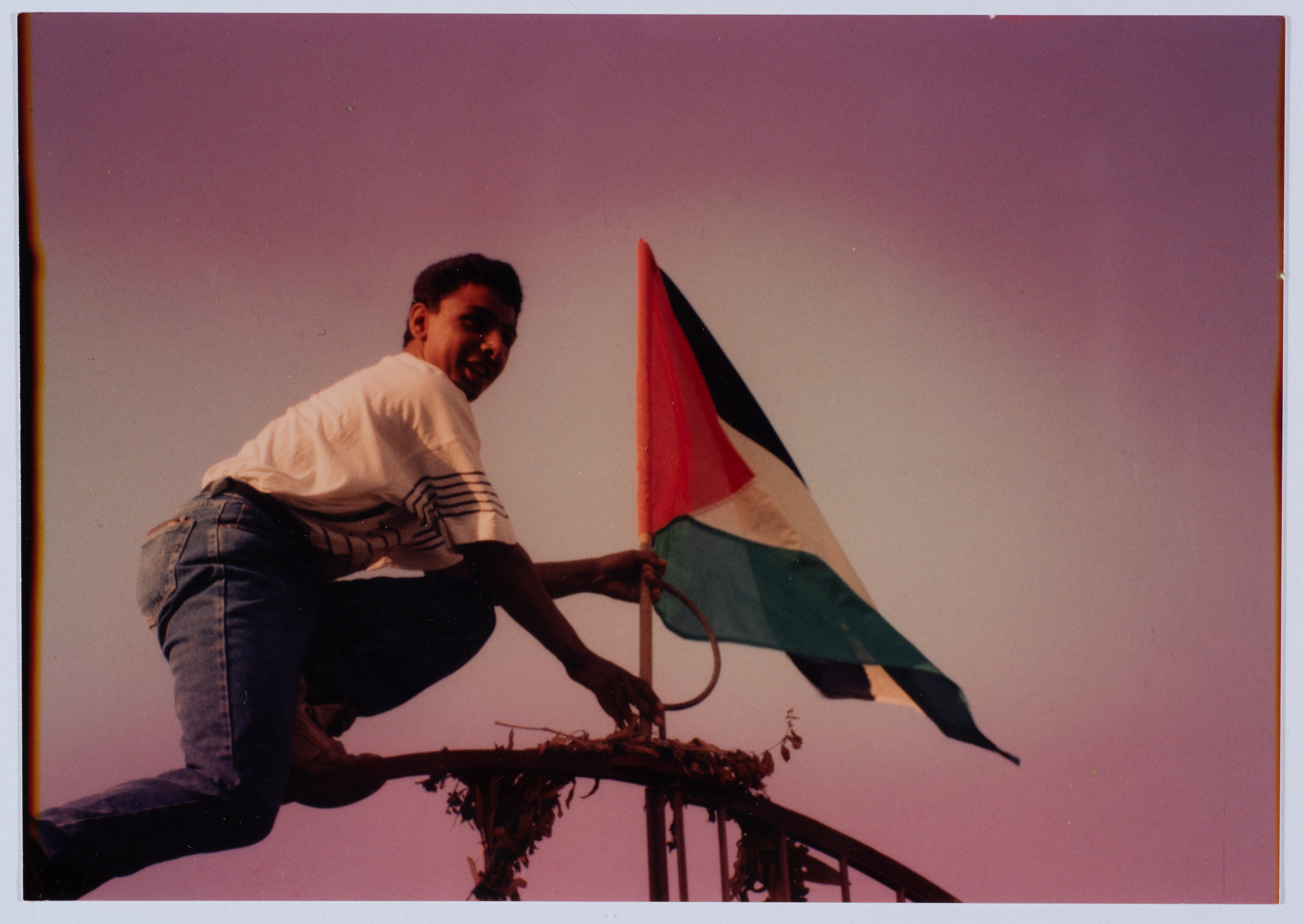 Un giovane innalza la bandiera palestinese sopra un traliccio elettrico nel campo profughi di Dheisheh (Nidal abu Aker, 1988-1989) - The Palestinian Museum Digital Archive